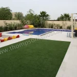 Swimming pool with tint mint paving, composite decking, metal sun shade structure, sunken seating zone with fire pit, artificial grass play zone.