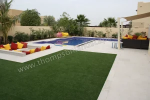 Swimming pool with tint mint paving, composite decking, metal sun shade structure, sunken seating zone with fire pit, artificial grass play zone.